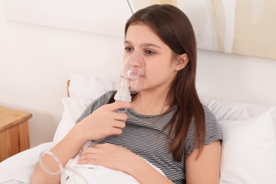 Photo of Cute girl using nebulizer for inhalation on bed at home