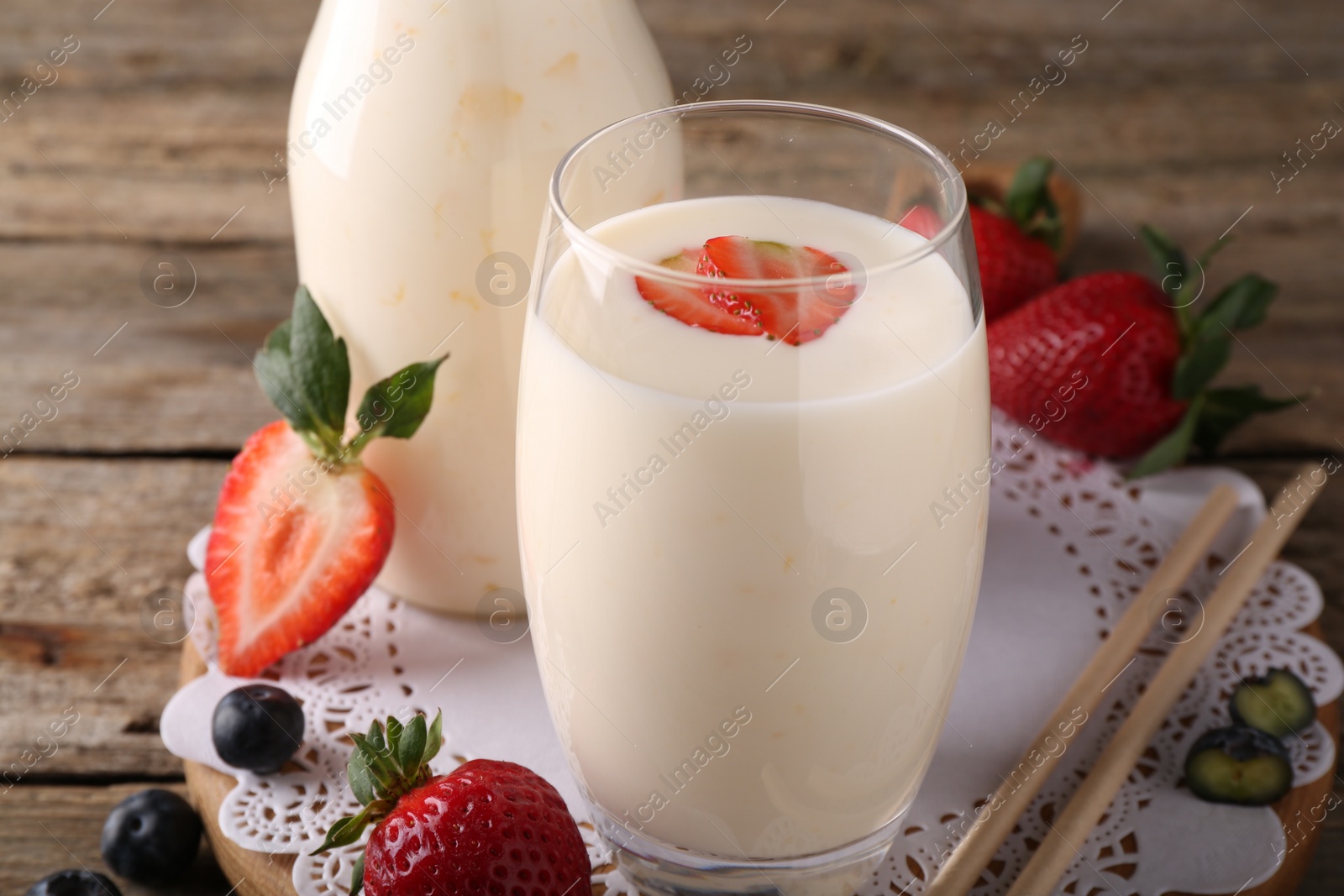 Photo of Tasty yogurt in glass, straws and berries on wooden table, closeup