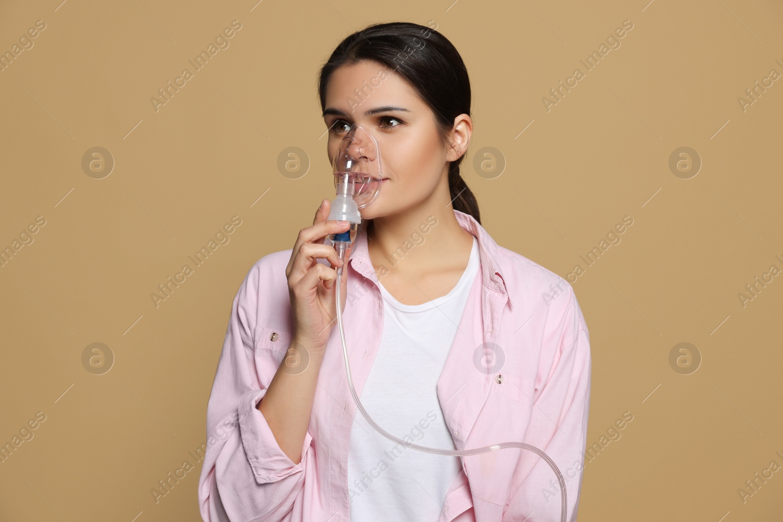 Photo of Sick young woman using nebulizer on dark beige background