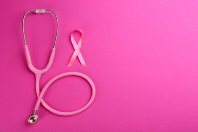 Photo of Pink ribbon as breast cancer awareness symbol and stethoscope on color background, flat lay. Space for text