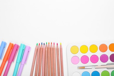 Photo of Watercolor palette, colorful pencils and markers on white background, flat lay. Space for text