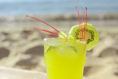 Photo of Glass of refreshing drink with kiwi and mint near sea, closeup