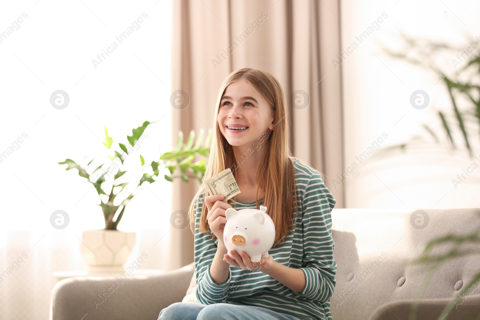 Photo of Teen girl with piggy bank and money at home