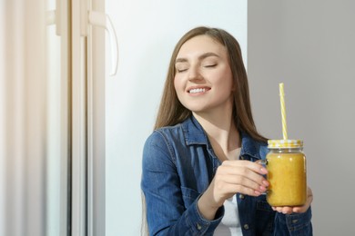 Beautiful young woman with delicious smoothie near window. Space for text