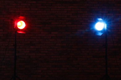 Photo of Bright blue and red spotlights near brick wall in dark room, space for text
