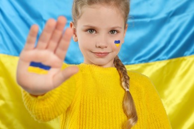 Photo of Little girl with paint on hand and face near Ukrainian flag