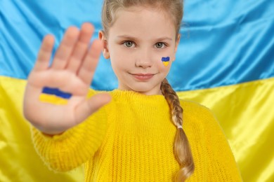 Photo of Little girl with paint on hand and face near Ukrainian flag