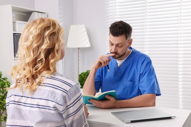 Photo of Doctor with notebook consulting patient at table in clinic