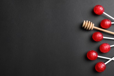 Photo of Many lollipops and honey dipper on black table, flat lay. Space for text