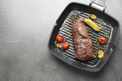 Photo of Delicious grilled beef meat and vegetables in pan on grey table, top view. Space for text