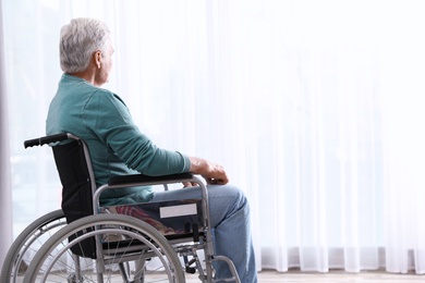 Senior man sitting in wheelchair near window at home