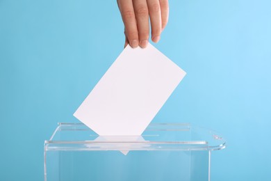 Photo of Woman putting her vote into ballot box on light blue background, closeup