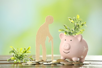 Photo of Pension savings. Figure of senior man, piggy bank, coins and green twigs on wooden table against blurred background