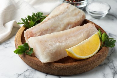 Photo of Fresh raw cod fillets with parsley and lemon on white marble table, closeup