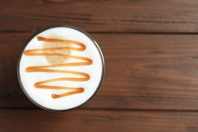 Photo of Glass with delicious caramel latte on wooden background