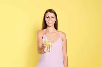 Photo of Young woman with glass of lemon water on yellow background