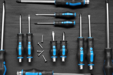 Photo of Set of screwdrivers and screws on black wooden table, flat lay