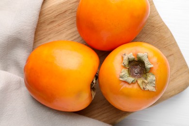 Photo of Board with delicious ripe persimmons on white wooden table, top view