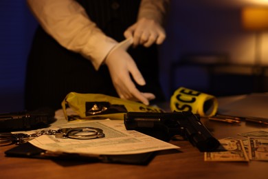 Photo of Professional detective in protective gloves working with evidence indoors at night, selective focus