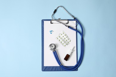Photo of Stethoscope, pills, nasal spray and clipboard on light blue background, top view. Medical tools