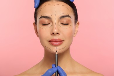 Photo of Doctor with pencil preparing patient for cosmetic surgery operation on pink background, closeup