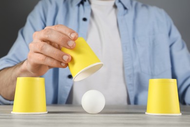 Photo of Shell game. Man showing ball under cup at wooden table, closeup