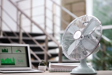Photo of Modern electric fan on table in office. Space for text