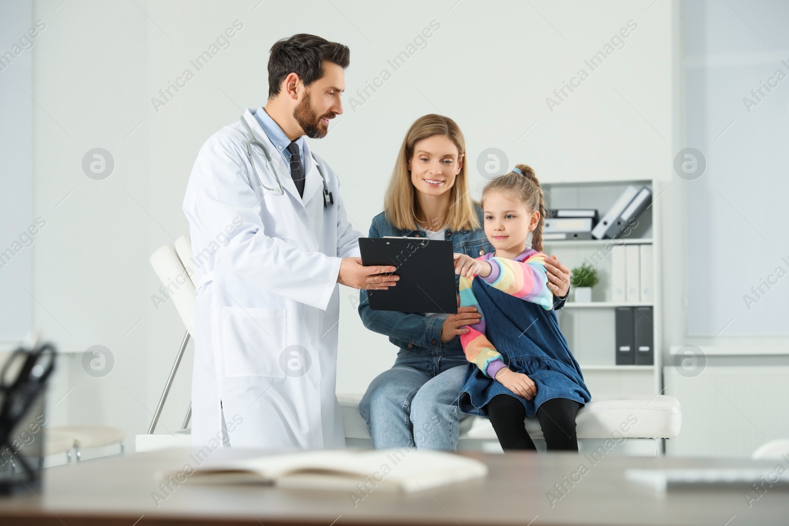 Photo of Happy mother and daughter having appointment with doctor. Pediatrician consulting patient in clinic