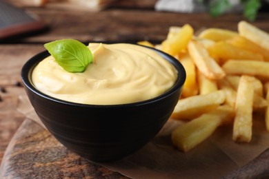 Photo of Delicious French fries and cheese sauce with basil on wooden table, closeup