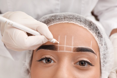 Photo of Young woman getting prepared for procedure of permanent eyebrow makeup in tattoo salon, closeup