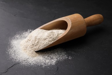 Photo of Wooden scoop with quinoa flour on black table