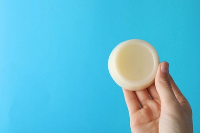 Photo of Woman holding solid shampoo bar against light blue background, closeup. Space for text