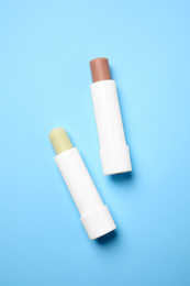 Photo of Hygienic lipsticks on light blue background, flat lay