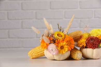 Photo of Compositionsmall pumpkins with beautiful flowers and corn cobs on light wooden table against white brick wall. Space for text