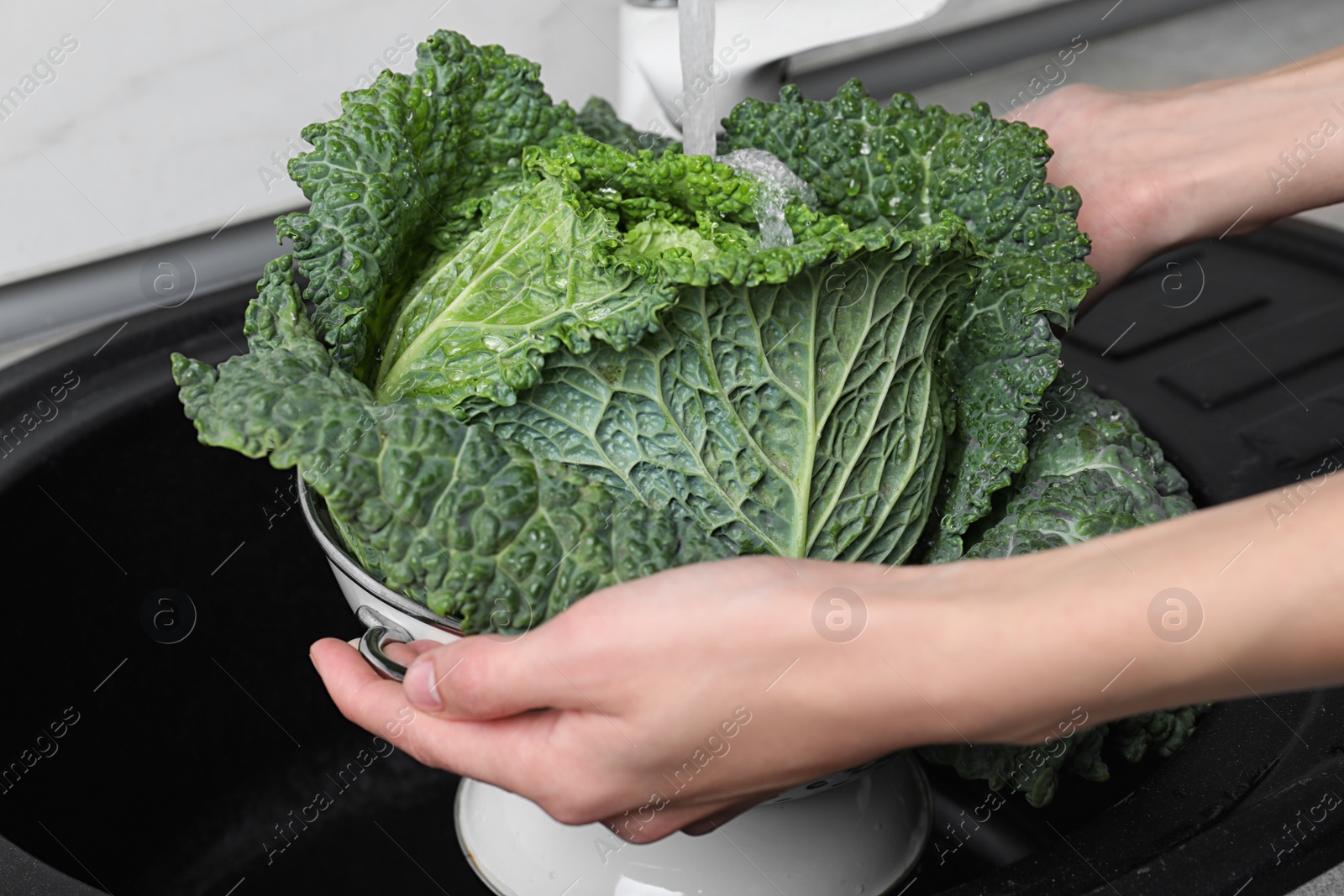 Photo of Woman washing fresh green savoy cabbage under tap water in kitchen sink, closeup