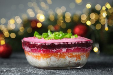 Photo of Herring under fur coat salad on grey table against blurred festive lights, closeup with space for text. Traditional Russian dish