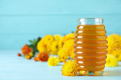 Photo of Tasty honey and chrysanthemum flowers on light blue table