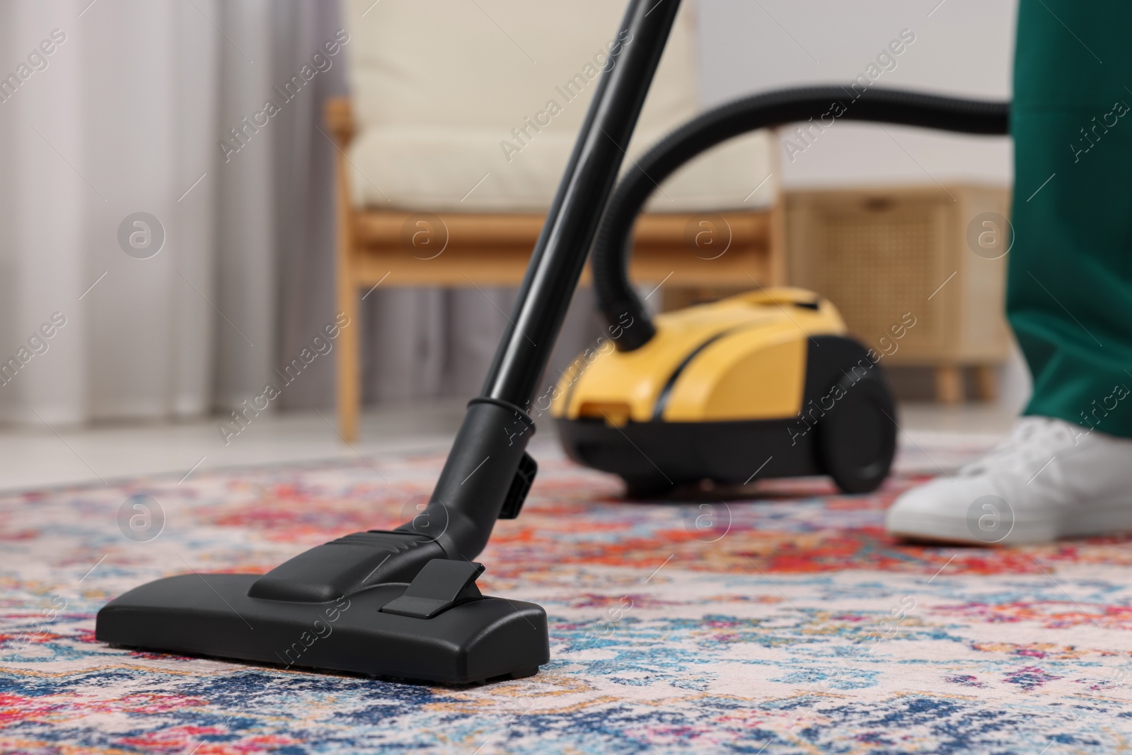 Photo of Dry cleaner's employee hoovering carpet with vacuum cleaner indoors, closeup