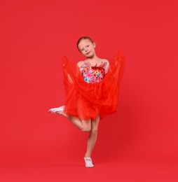 Photo of Cute little girl dancing on red background, space for text