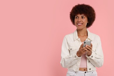 Photo of Happy young woman with smartphone on pink background. Space for text