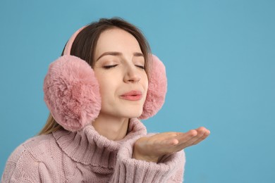 Photo of Happy woman wearing warm earmuffs on light blue background