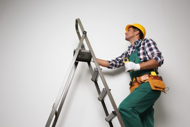 Photo of Professional builder climbing up metal ladder on light background