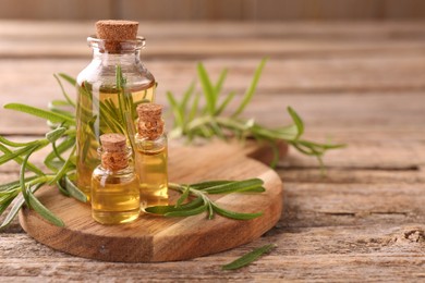 Photo of Aromatic essential oils in bottles and rosemary on wooden table, closeup. Space for text