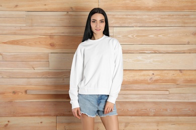 Photo of Portrait of young woman in sweater at wooden wall. Mock up for design