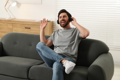 Photo of Happy man listening music with headphones on sofa indoors