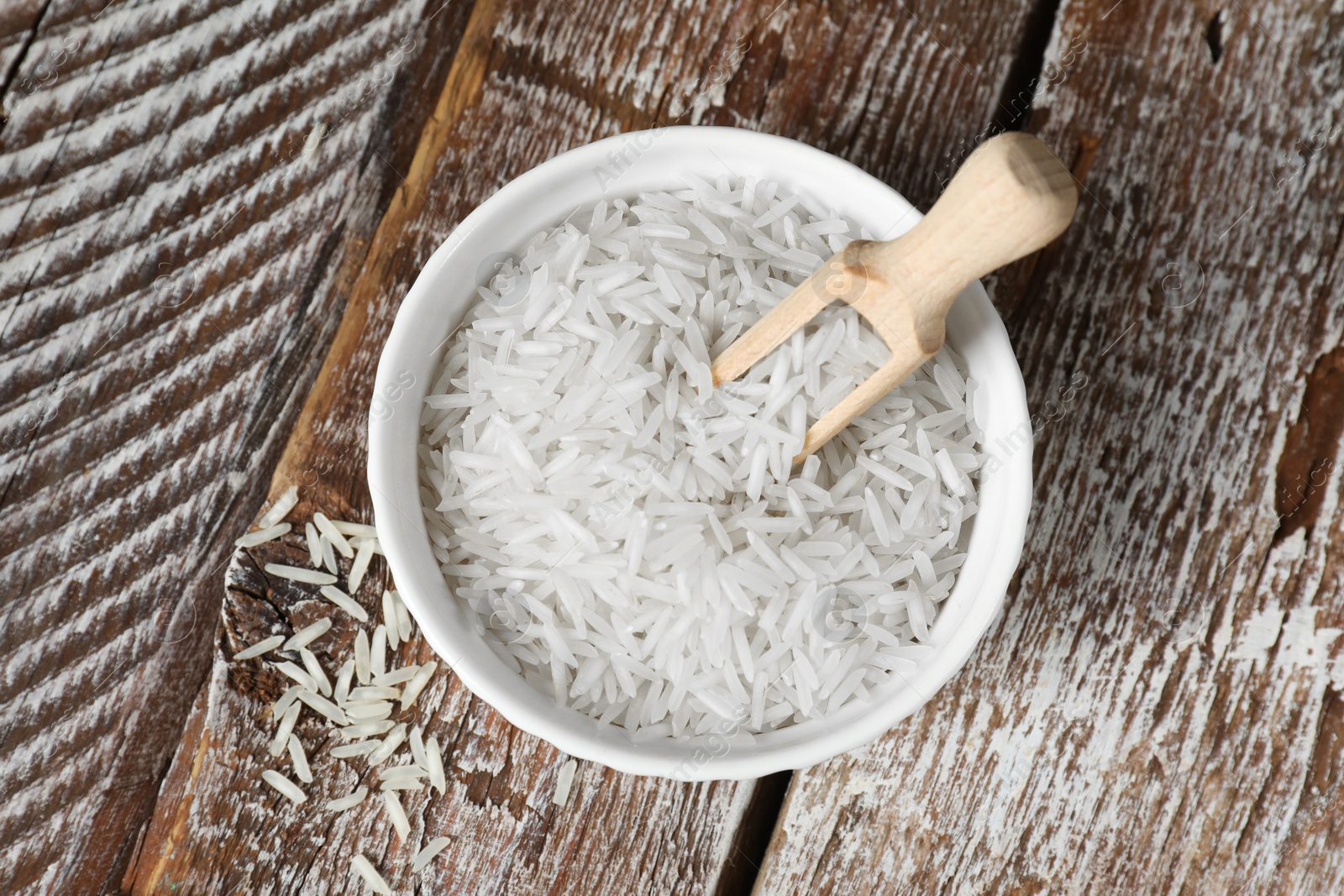 Photo of Raw basmati rice in bowl and scoop on wooden table, top view