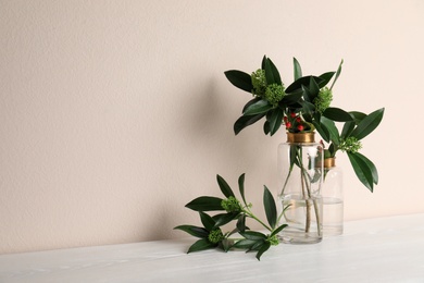 Photo of Vases with beautiful branches on white wooden table near beige wall. Space for text