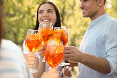 Photo of Friends clinking glasses of Aperol spritz cocktails outdoors, focus on hands