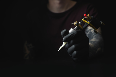 Photo of Tattoo artist with professional machine at table against black background, closeup