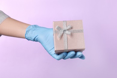 Photo of Doctor holding gift box on violet background, closeup. Medical present